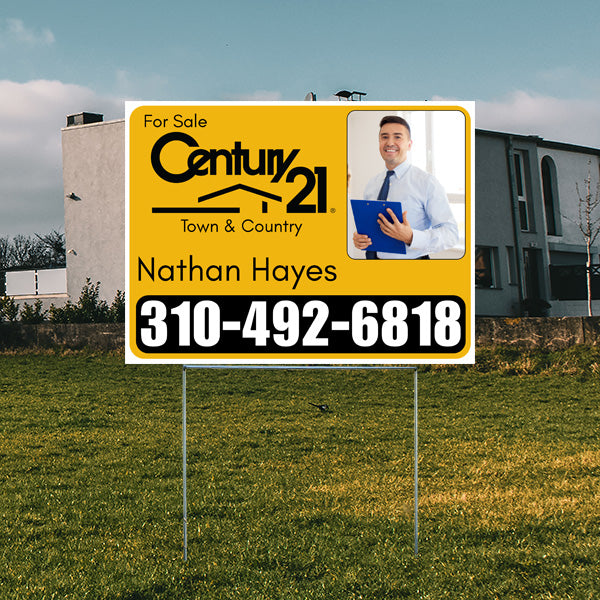 Real estate for sale sign by Century 21 Town & Country, featuring agent photo and contact number 310-492-6818, placed on a lawn with a modern house in the background.
