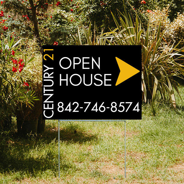 Real estate open house sign with contact number in a garden setting.