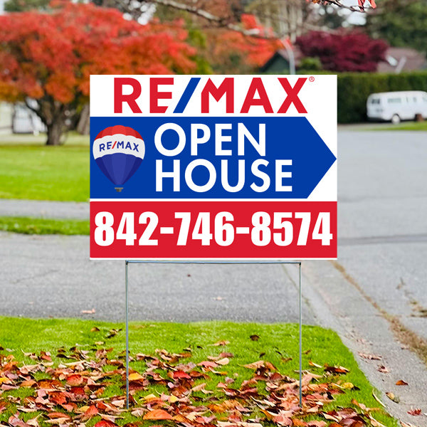 Real estate open house sign with RE/MAX branding and contact number on a residential street with autumn leaves.