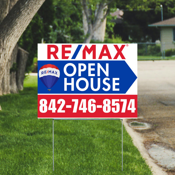 RE/MAX open house sign with contact number 842-746-8574 displayed on a lawn near trees and a driveway.