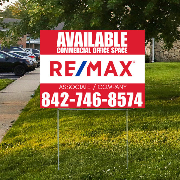 Real estate sign for available commercial office space, RE/MAX logo, contact number 842-746-8574, displayed on grass with trees and parked cars in the background.