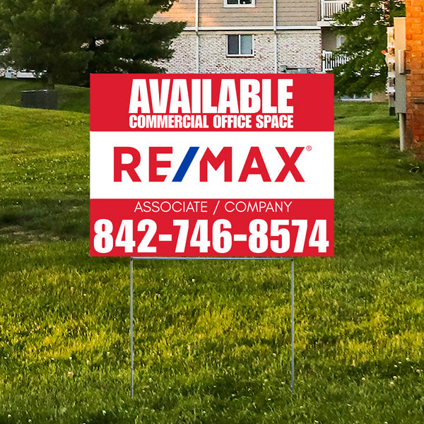 Real estate sign advertising available commercial office space by RE/MAX with contact number 842-746-8574, placed on green grass in front of residential buildings.