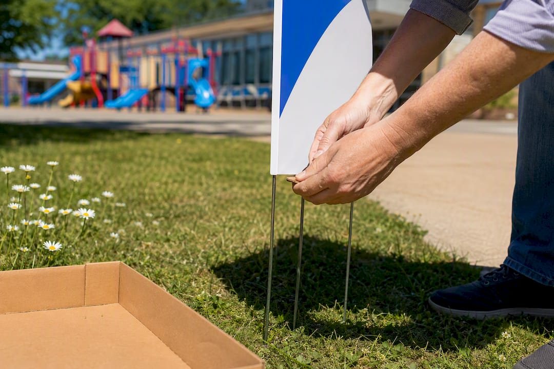 Hands installing school event yard sign outdoors