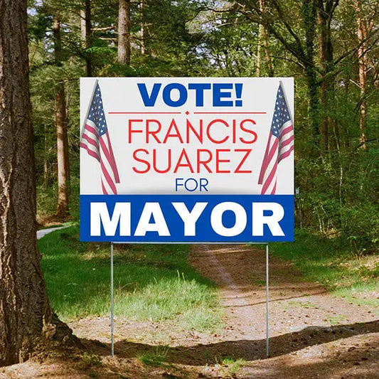 Political campaign yard sign displayed in wooded path.