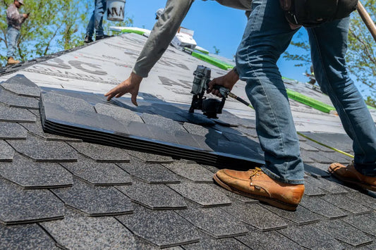 Roofer installing shingles with nail gun on roof.