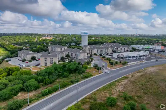 Aerial view of a suburban area with residential buildings and greenery under a blue sky.