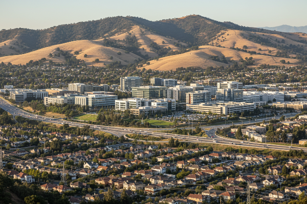 Cityscape with buildings and roads, surrounded by hills and mountains.