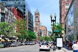 City street scene with tall buildings, cars, and pedestrians on a clear day.