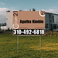 Real estate sign for Century 21 agent Agatha Kimble with contact number 310-492-6818, displayed on a grassy lawn in front of a modern house.