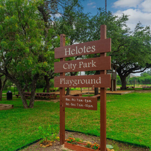 Sign for Helotes City Park Playground with trees and grass in the background