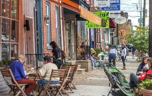 People dining outdoors on a city street with storefronts and pedestrians in the background.