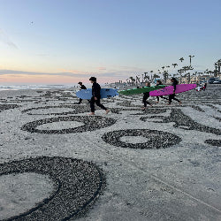 People walking on a beach with surfboards, palm trees in the background