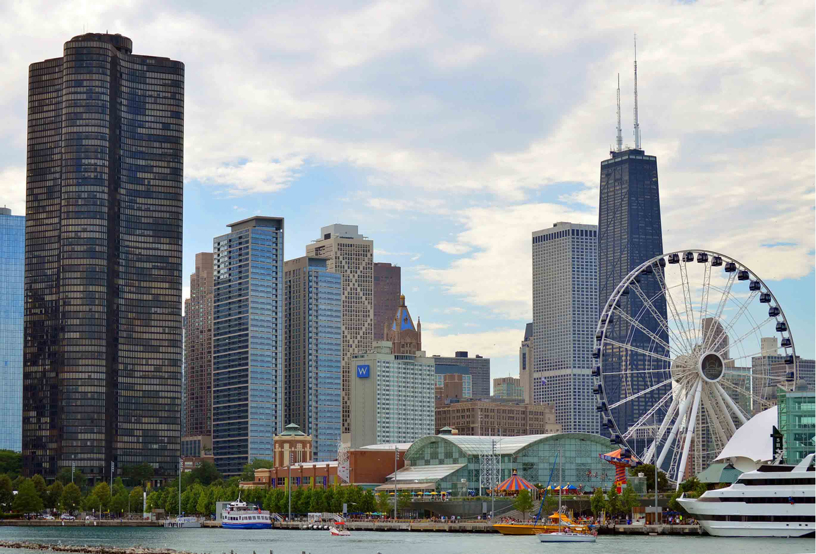 City skyline with skyscrapers and a Ferris wheel on a partly cloudy day.