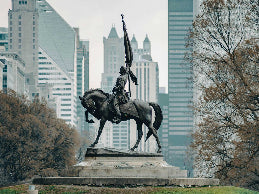 Statue of a person on horseback in a park with tall buildings in the background